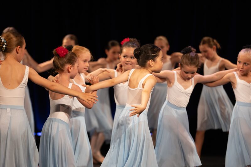 Group of Ananyan Ballet students in white tops and pale blue skirts performing on stage.